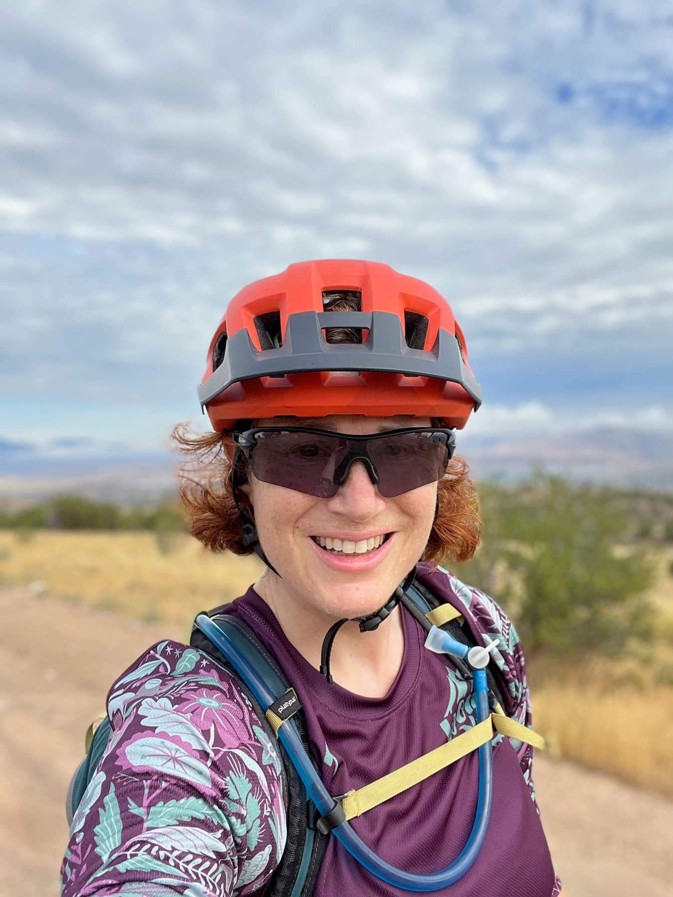 Ann in mountain bike kit, helmet and sunglasses, desert backdrop.